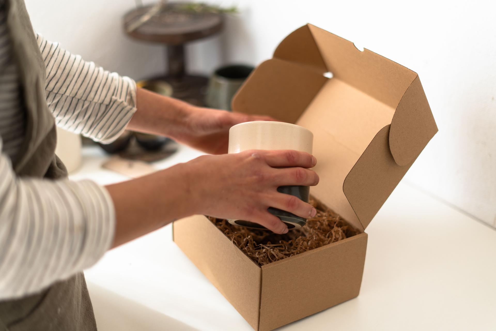 Ceramist carefully packaging handmade mug for shipping in cardboard box